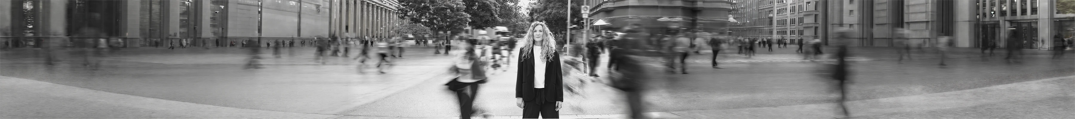 Nadja Hollstein blickt ruhig in die Kamera, während Menschen um sie herum in Bewegung sind.